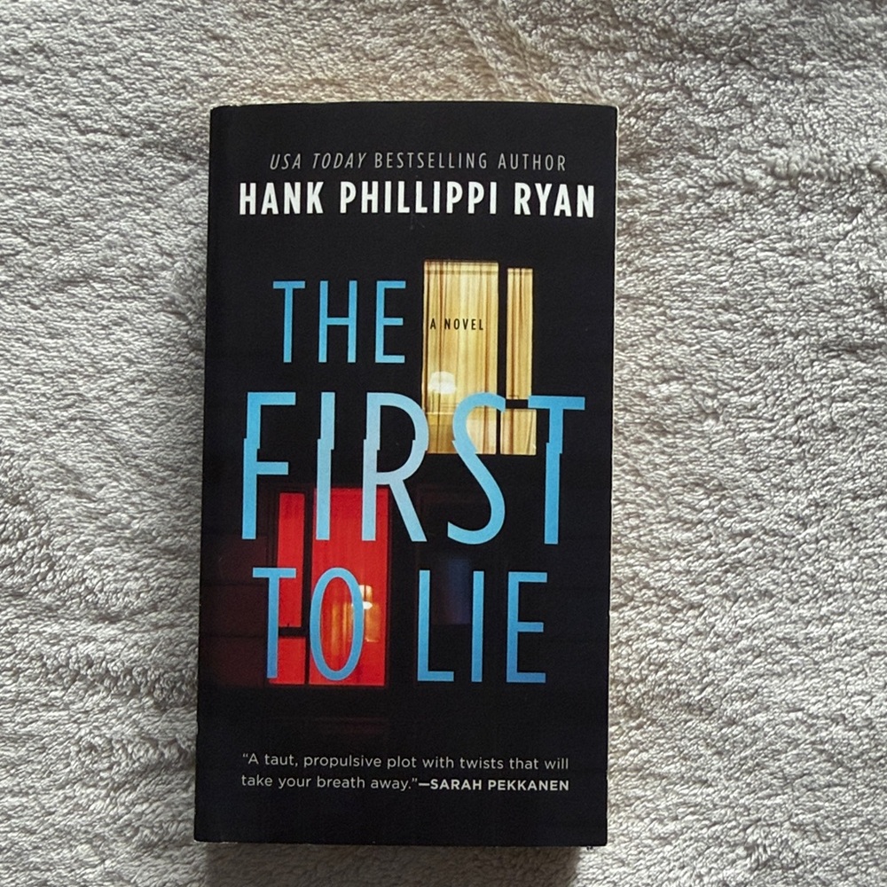 The First to Lie by Hank Phillippi Ryan - Black Cover with Blue & Red Accents